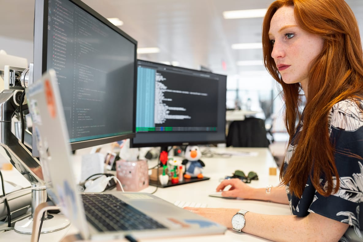 Woman in office programming on her laptop and two extra monitors